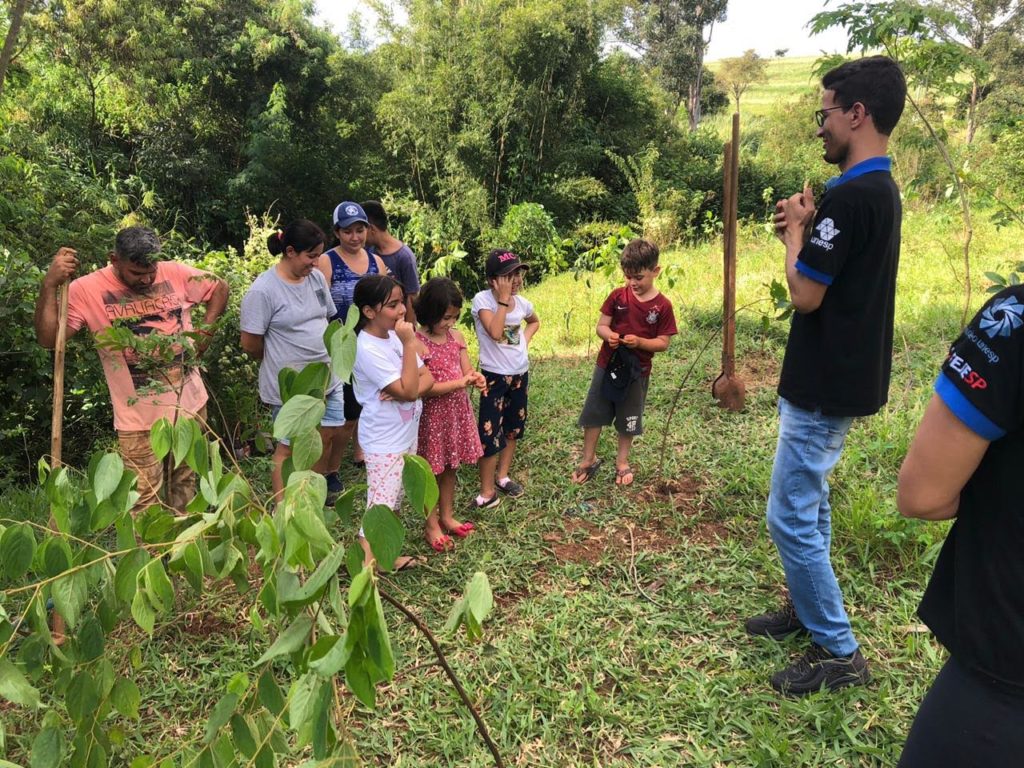 Um adulto conversando com um grupo de crianças perto da natureza. Educação ambiental.